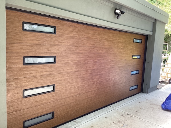 High-end wood-grain garage door with horizontal lines and multiple window inserts installed on a contemporary home in Carmel, Indiana.