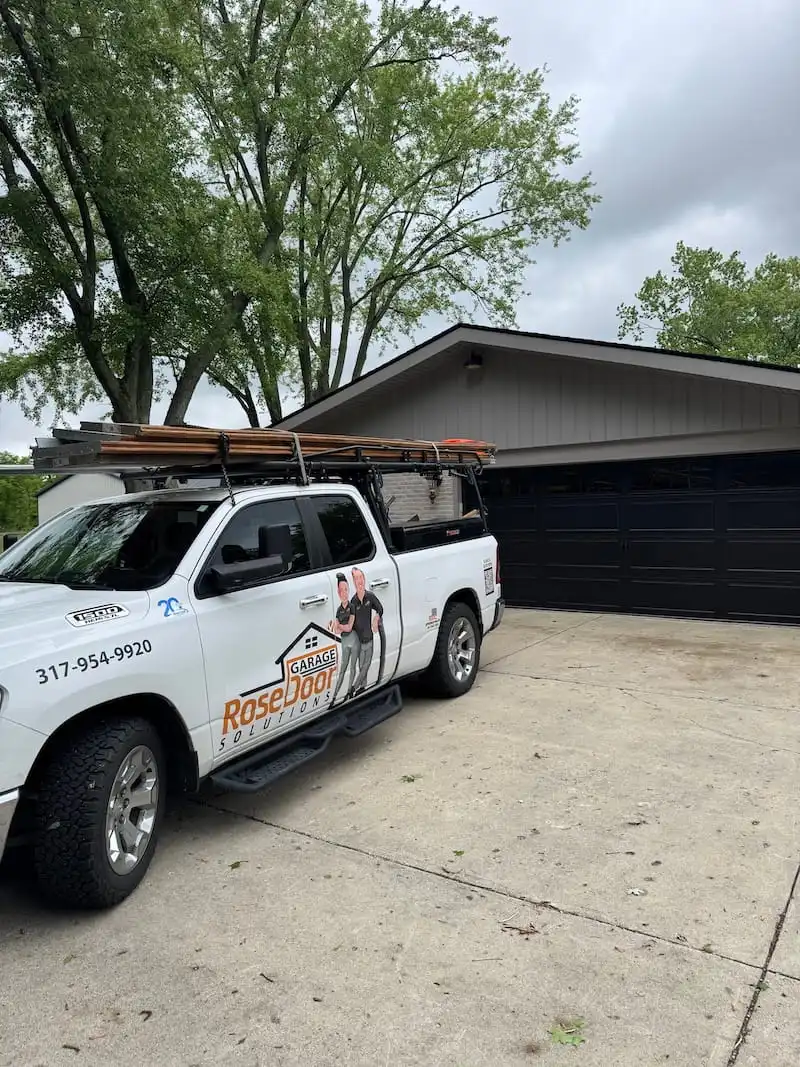 Rose Garage Door Solutions service truck loaded with equipment parked in front of navy blue garage doors on a home in Carmel, IN