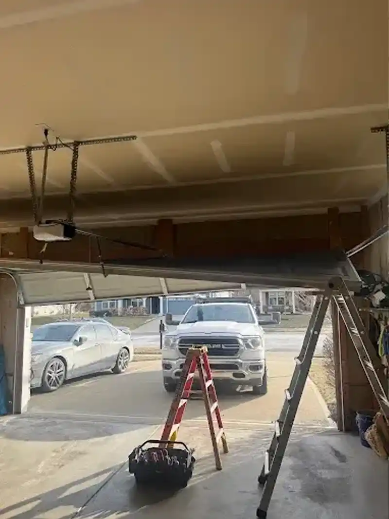 A broken garage door in need of repair with Rose Garage Door Solutions truck in teh background
